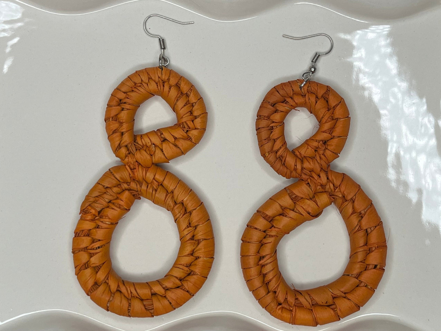 Pair of woven brown earrings on a white decorative plate.