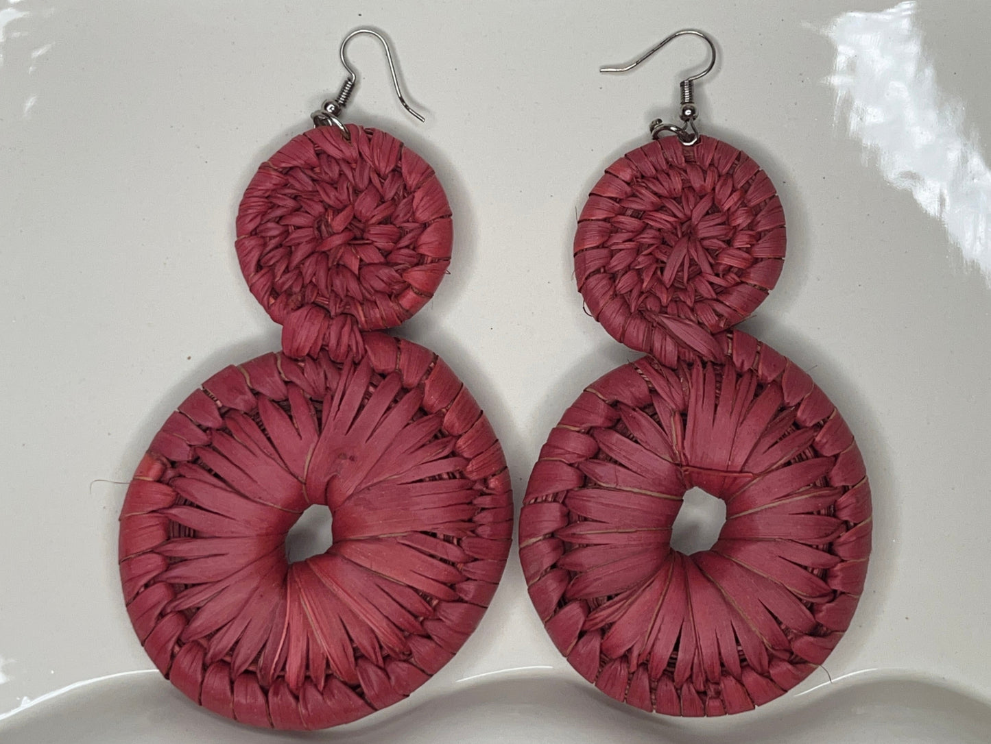 Pink raffia earrings on a white decorative plate.