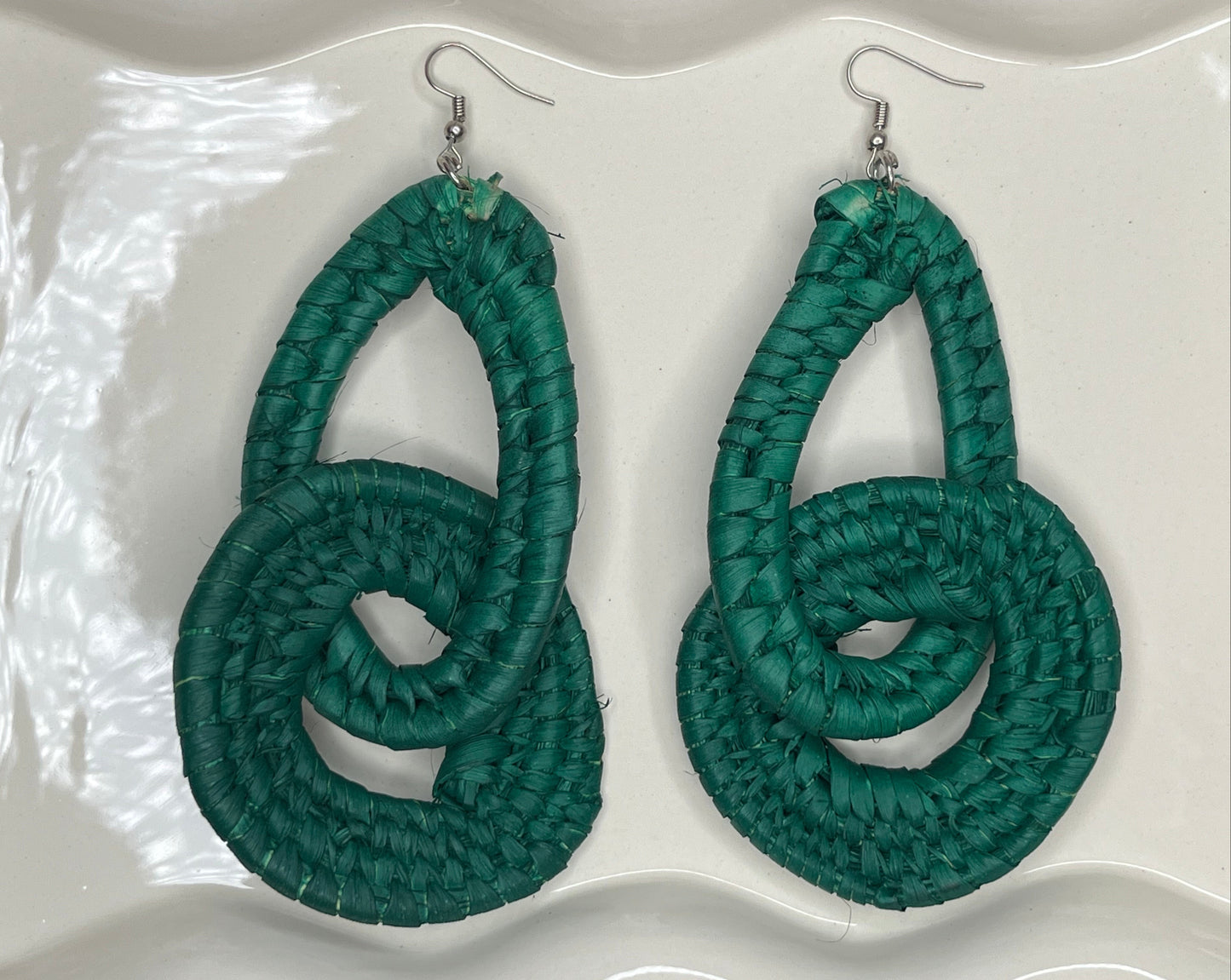 Pair of green knotted raffia earrings on a white background