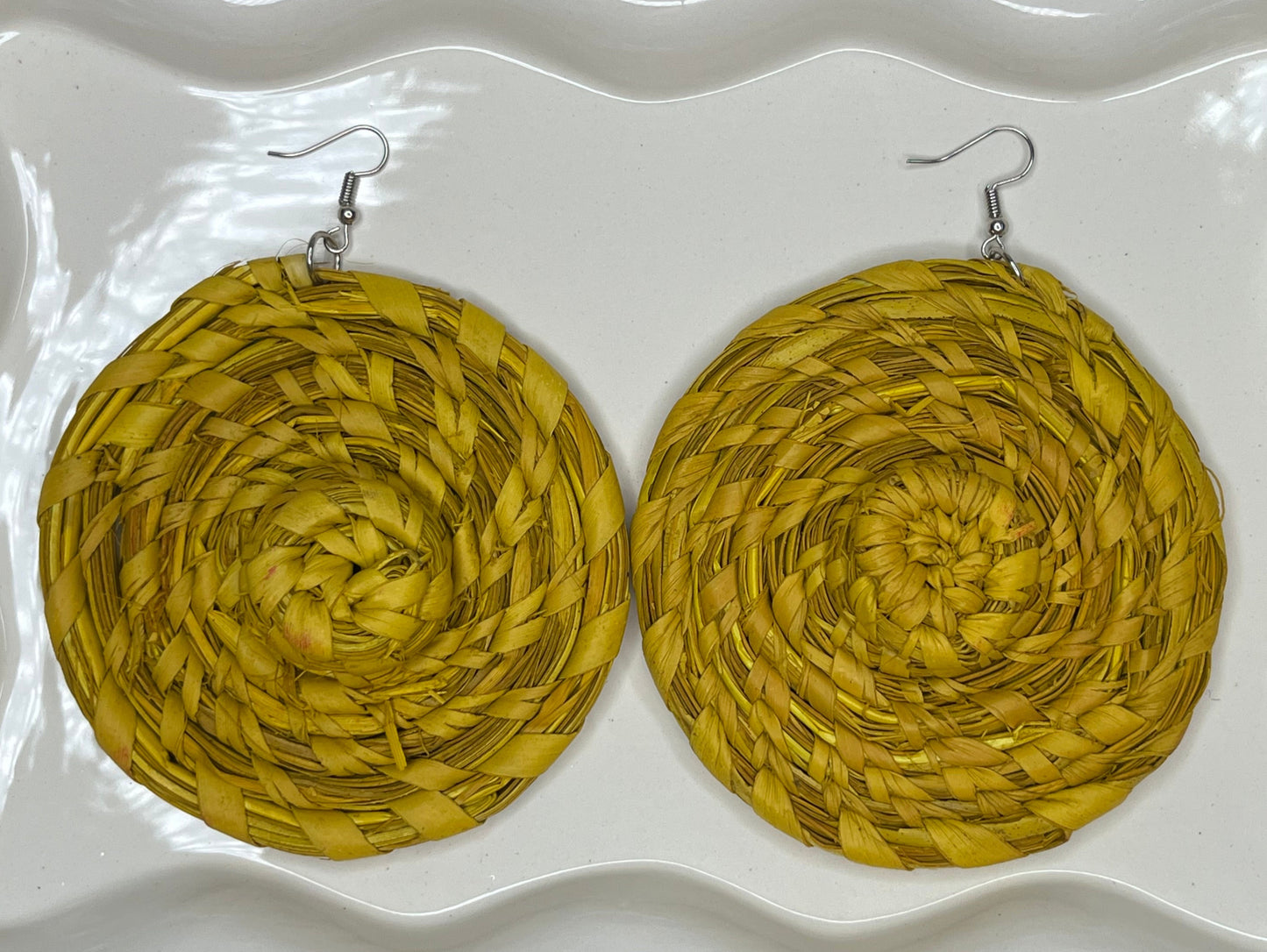 Yellow raffia circular earrings on a white decorative plate.
